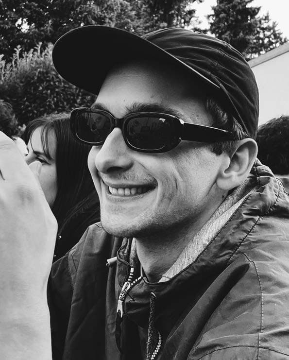 Schwarz-Weiß-Porträt von Max Maicher mit Cap und Sonnenbrille, lachend im Freien